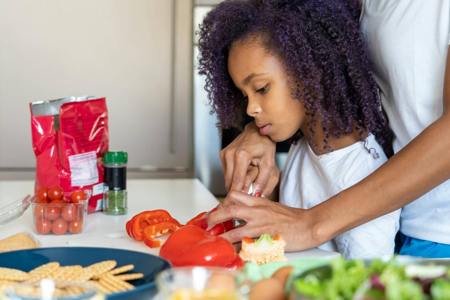 https://www.pexels.com/photo/a-parent-helping-a-girl-slice-a-bell-pepper-6297627/